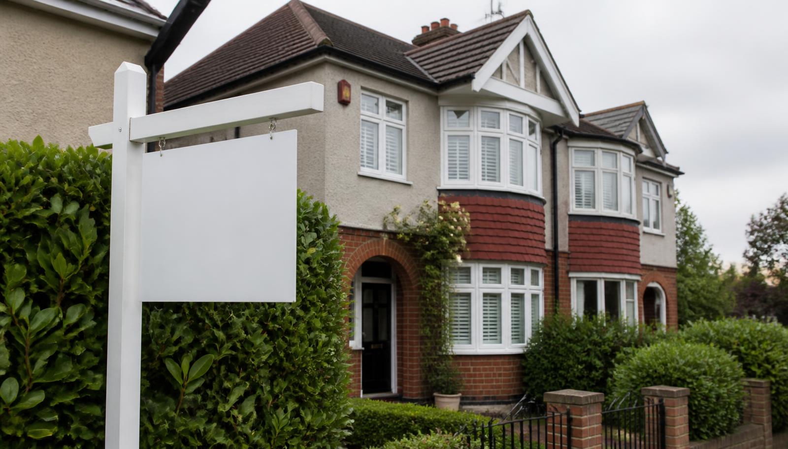 A blank estate agent for-sale board outside a British semi-detached house