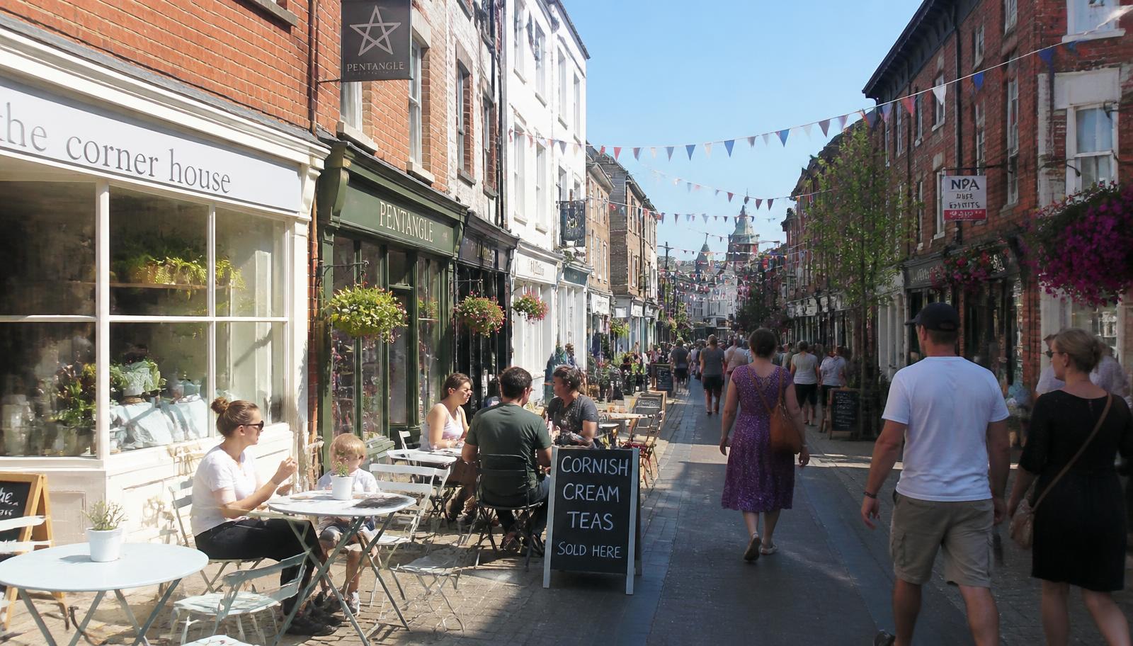 A busy British high street with independent shops and a cafe with outdoor tables