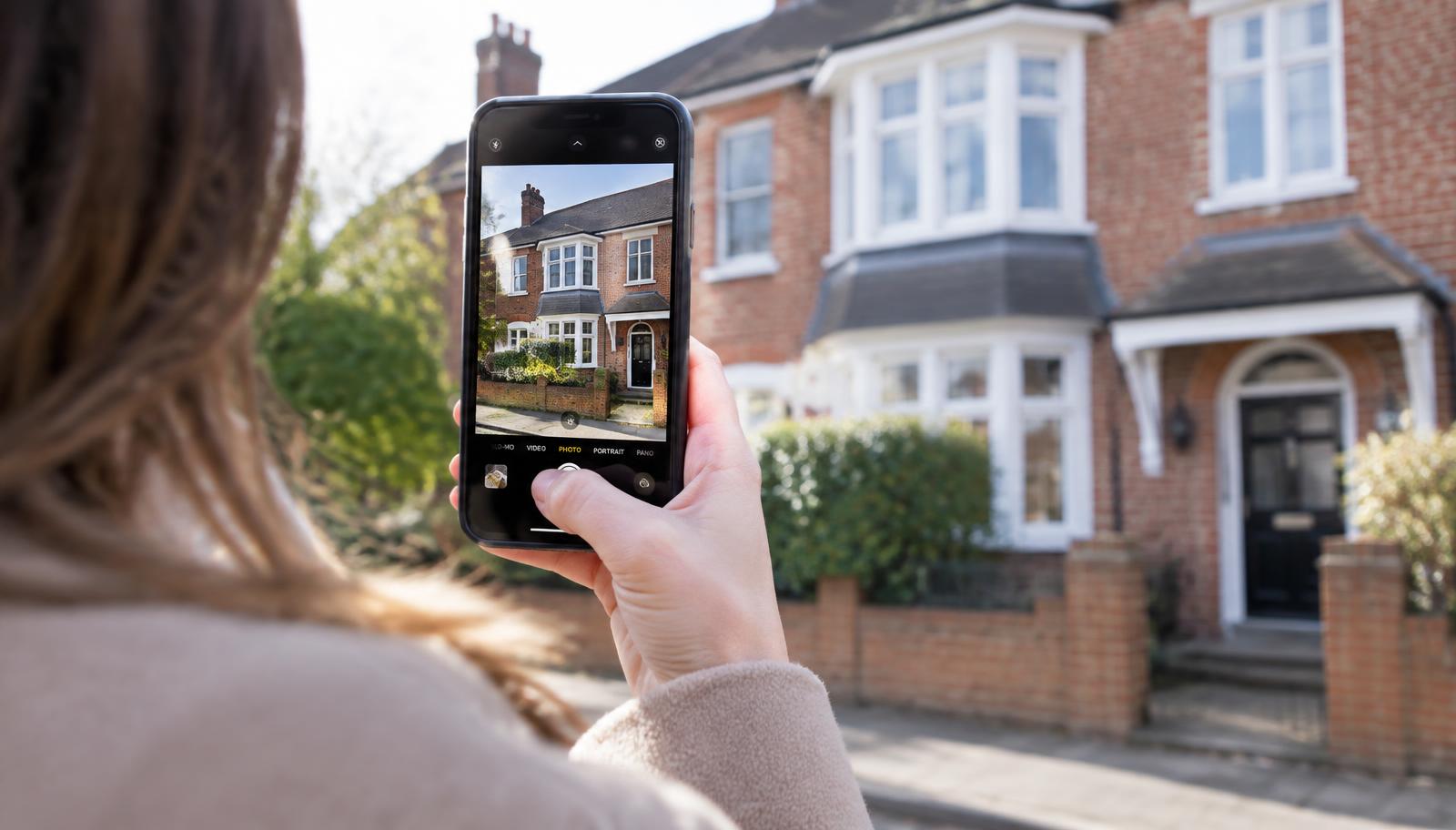 Person photographing a British semi-detached house with a smartphone